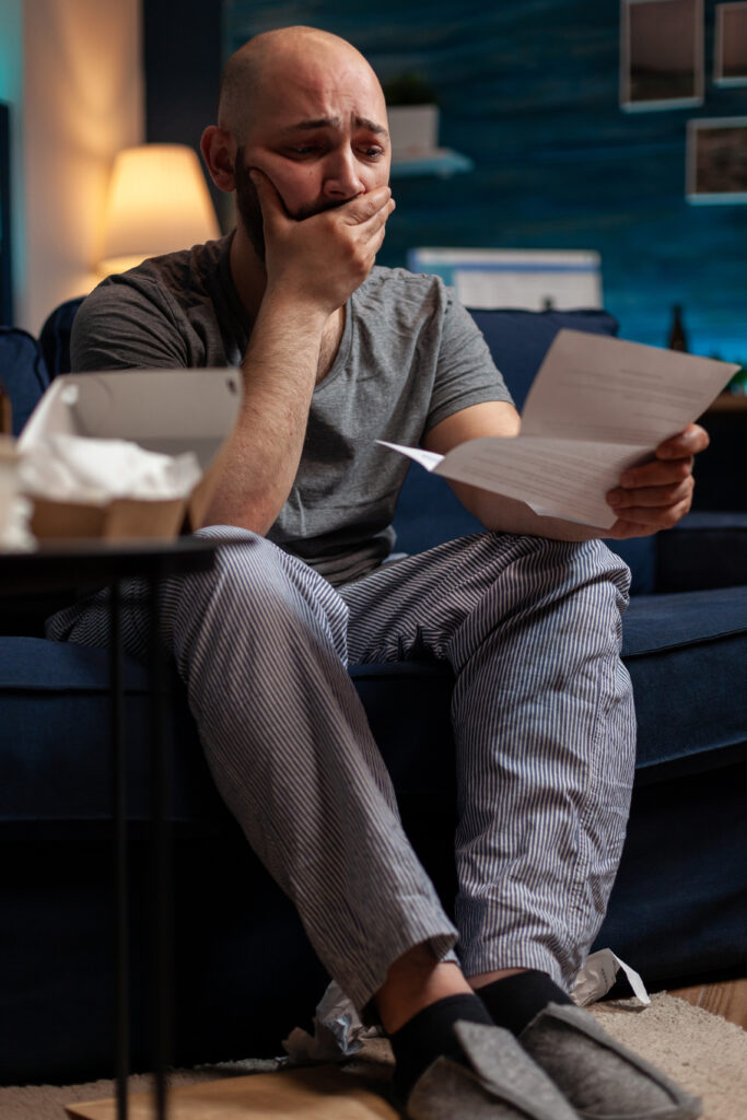 Desperate frustrated adult worrying about eviction notice letter, feeling sad about financial crisis. Anxious man with chronic depression having to pay taxes, reading bank warning paper.